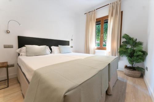 a white bedroom with a large bed and a plant at Houm Villa Nets in Playa de Palma