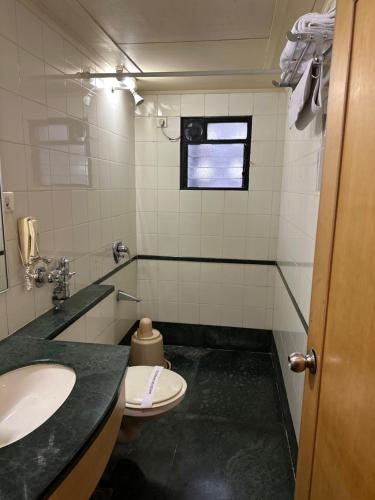 een badkamer met een wastafel, een toilet en een raam bij Hotel Ashirwad in Pune