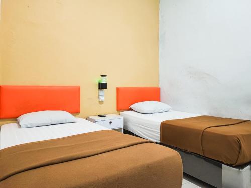 two beds in a room with orange and white at Reddoorz @ Hotel Bersaudara Bungo in Muarabungo