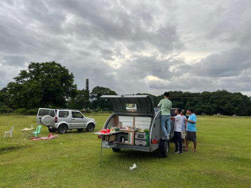 un grupo de personas de pie en un campo cerca de un vehículo en Camping car room 