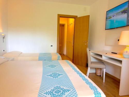 a room with two beds and a desk and a table at Hotel Dei Pini in Alghero