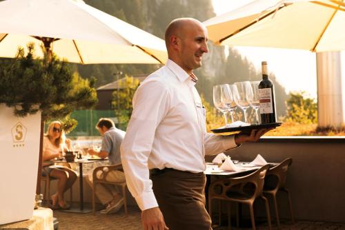 un hombre sosteniendo una bandeja con una botella de vino en Gästehaus by Stoos Hotels, en Stoos