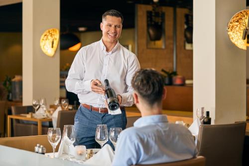 a man pouring a man a glass of wine in a restaurant at Gästehaus by Stoos Hotels in Stoos