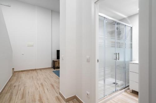 una doccia in vetro in una camera bianca con pavimento in legno di amplio duplex reformado a Madrid