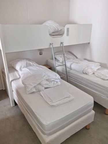 - 2 lits dans une chambre avec des draps blancs et des serviettes dans l'établissement Location d'un mobil-home de 35 m² au Camping Les Sables d'Or - 4 étoiles avec grand parc aquatique, au Grau-dʼAgde