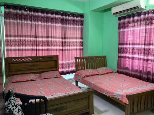two beds in a room with pink curtains at Mohammadia Restaurant & Guest House in Dhaka