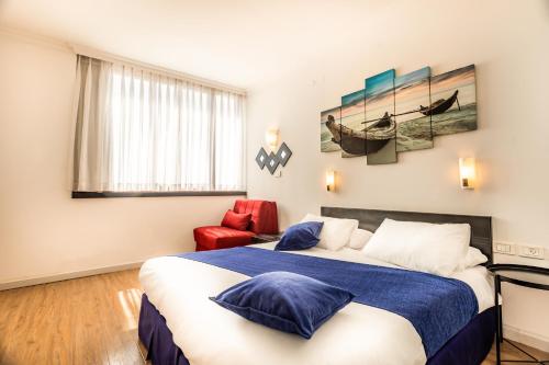 Habitación de hotel con cama y silla roja en Inbar Hotel en Arad