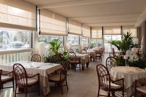 restauracja z białymi stołami, krzesłami i oknami w obiekcie Grand Hotel & Riviera w mieście Lido di Camaiore