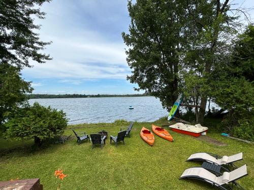 a group of chairs and kayaks on the grass near a lake at Modern, Sunset Waterfront Cottage with EV Charger in Yarker