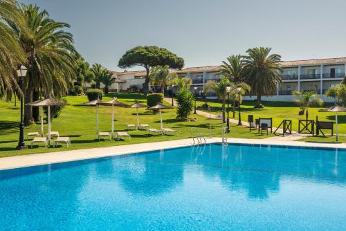 a swimming pool with chairs and umbrellas and a building at Parador de Mazagón in Mazagón