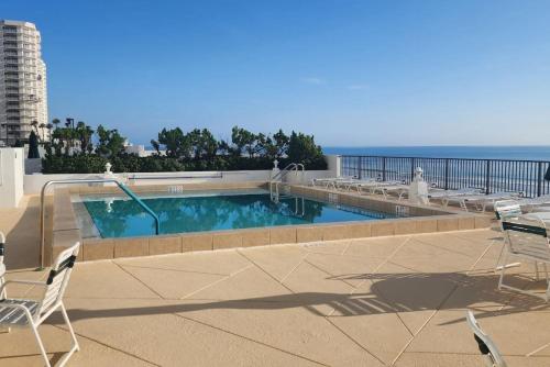a swimming pool with chairs and the ocean in the background at Coastline Penthouse Condo in Daytona Beach Shores
