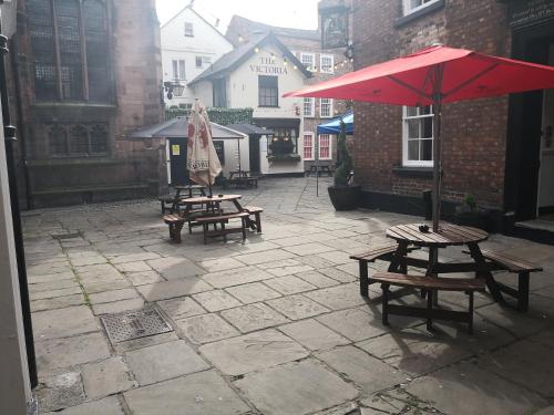 dos mesas de picnic y una sombrilla roja en un patio en The Commercial Bar & Hotel en Chester