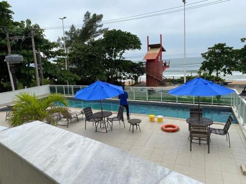 uma piscina com mesas, cadeiras e guarda-sóis azuis em Flat em frente a praia Macaé em Macaé