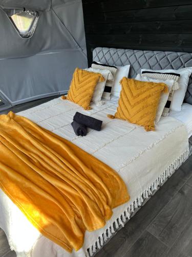 uma cama grande com lençóis e almofadas amarelos e brancos em Skywoods.glamping em Molėtai