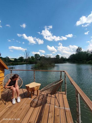 a woman sitting on a deck with a table and a bench at Les Cabanes Flottantes in Givrauval