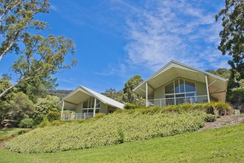 カンガルー・バレーにあるKangaroo Valley Golf and Country Retreatの木々と芝生の丘の上の家