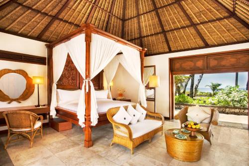 The Oberoi Beach Resort, Bali في سمينياك: غرفة نوم بها سرير مظلة وأريكة وكراسي