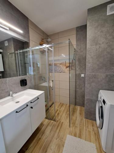 La salle de bains est pourvue d'un lavabo blanc et d'une douche. dans l'établissement Bursztynowy dom Międzywodzie Apartament z 1 sypialnią, à Międzywodzie