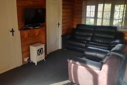 a living room with a leather couch and a flat screen tv at Cabin in Trawsfynydd