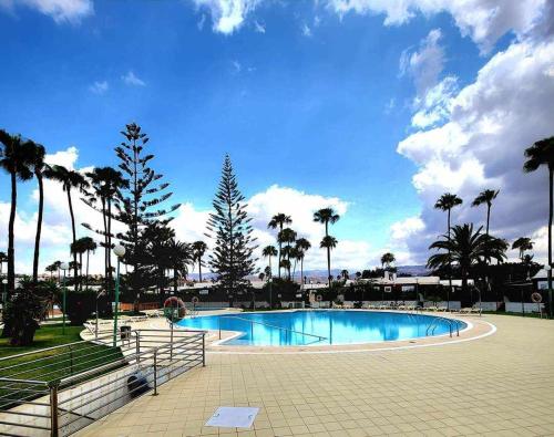 una grande piscina con palme in un parco di Chalet con 3 camere e giardino a Maspalomas