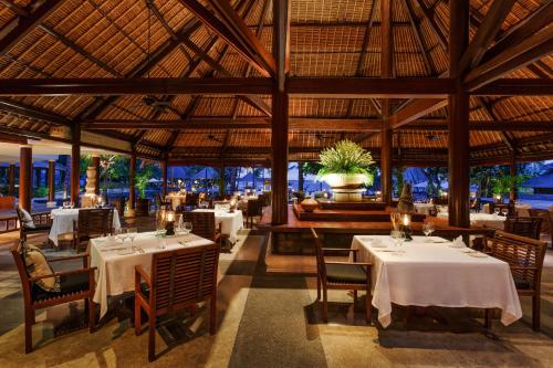 a restaurant with white tables and chairs and a large ceiling at The Oberoi Beach Resort, Lombok in Tanjung
