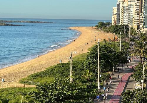 a beach with people walking on it next to the ocean at Apartamento Renovado na beira da Praia in Vila Velha