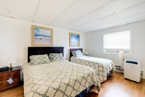 two beds in a bedroom with white walls and wood floors at Hannahs Place - Quaint and Cozy Apt by the Beach! in Emerald Isle