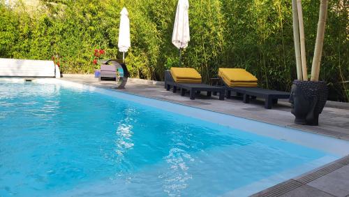 - une piscine avec 2 chaises longues et des parasols dans l'établissement Le mas ROLLAND - Piscine & SPA - MILLAU-GORGES du TARN, à Compeyre