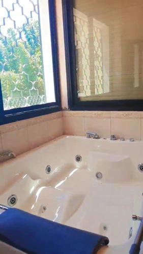 La salle de bains est pourvue d'une baignoire blanche et de 2 fenêtres. dans l'établissement Villas avec Piscine & Jardin Privés, à Marrakech