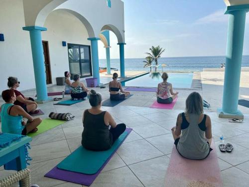 a group of people sitting in a yoga pose by the beach at Villa Star of the Sea in Barra de Navidad