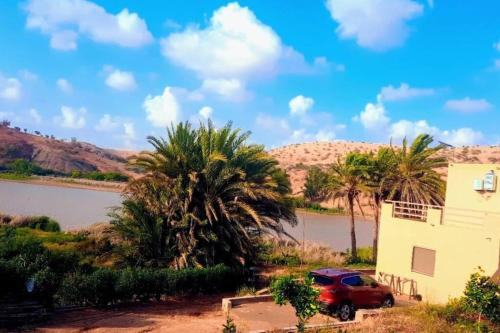 a red car parked next to a building and palm trees at Lake House Boulaouane in El Jadida
