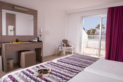 a bedroom with a bed and a desk and a window at New Famagusta Hotel & Suites in Ayia Napa