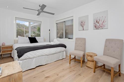 a white bedroom with a bed and two chairs at Collaroy Beachfront Escape - New Listing in Collaroy