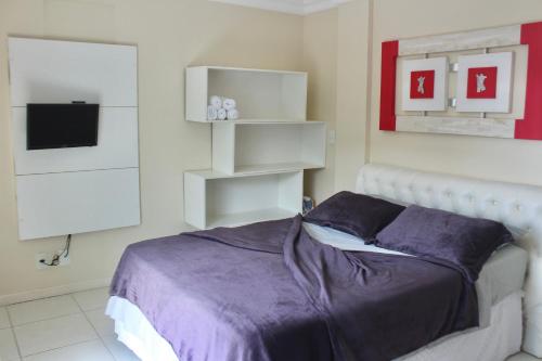 um quarto com uma cama com lençóis roxos e uma televisão em Charmoso Apartamento Arraial do Cabo em Arraial do Cabo