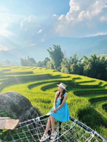 a woman in a blue dress sitting on a bridge in a field at En Hotel Sapa in Sa Pa