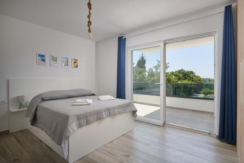 a white bedroom with a bed and a sliding glass door at Apartments Endji in Čilipi