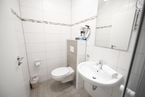 a white bathroom with a toilet and a sink at Hotel Wurster Kroog in Bremerhaven