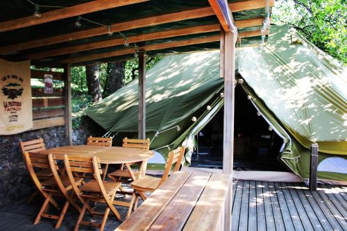 une table et des chaises en bois sur une terrasse avec un parasol dans l'établissement TENTE HERISSON BOHEME 4 PERSONNES Camping Lou cantou Cévenol, à Anduze