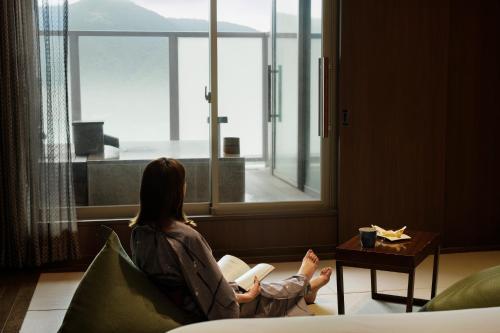 a woman sitting in a chair reading a book looking out the window at Laforet Hakone Gora Yunosumika in Hakone