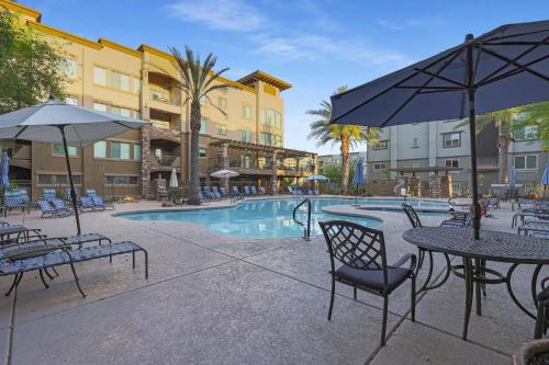 a swimming pool with tables and chairs and an umbrella at Villa Toscana condo in Phoenix