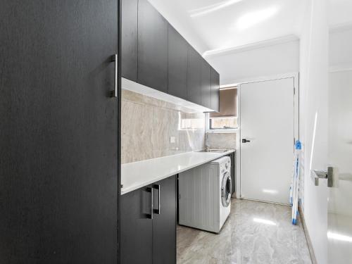 a kitchen with black cabinets and a washer and dryer at Sara by Ready Set Stay in Caroline Springs