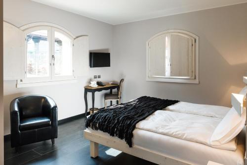 a bedroom with a bed and a chair and two windows at Bianco Hotel in Primaluna