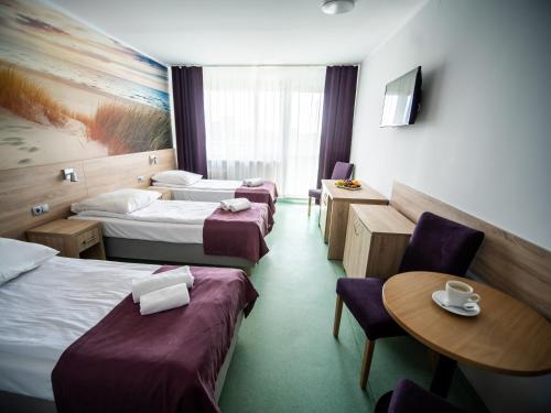 コウォブジェクにあるSanatorium Perla Baltykuのベッド3台、テーブル、椅子が備わるホテルルームです。