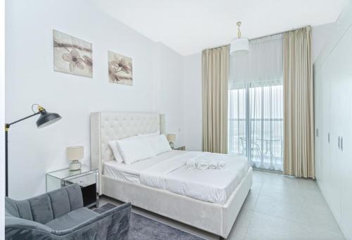 a white bedroom with a bed and a chair at Modern Studio with Pool & Gym Access in Dubai