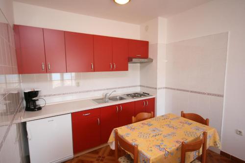 cocina con armarios rojos, mesa y fregadero en Apartments and rooms by the sea Pag - 6311 en Pag