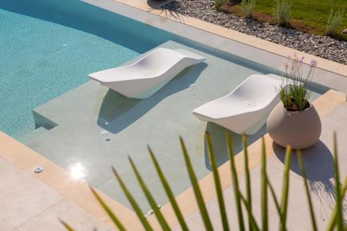 a pool with two white chairs and a vase at Song of the Sea in Sivota