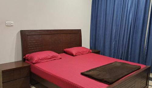 1 dormitorio con 1 cama con sábanas rojas y cortinas azules en The Guest House Islamabad, en Islamabad