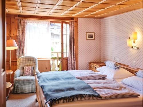 a bedroom with two beds and a chair and a window at Hotel Chesa Grischuna in Klosters