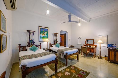 een slaapkamer met 2 bedden, een tafel en een bureau bij Neemrana's - Deo Bagh in Gwalior