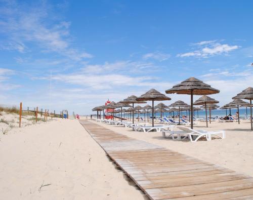 a boardwalk with chairs and umbrellas on a beach at Pedras Da Rainha in Cabanas de Tavira